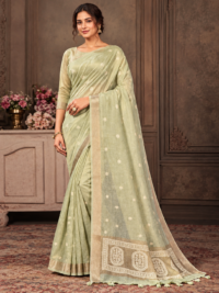 Model wearing a light sage-green saree with small floral motifs, a gold-tone border and a decorative tasselled pallu.